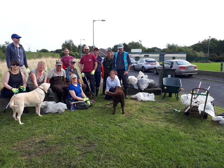 A group of 12 people and 2 dogs standing in a field in front the litter they collected from a nearby river